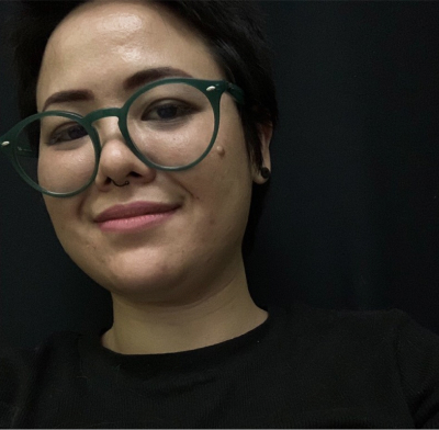 Alinny tem cabelos curtos preto. Usa óculos de grau preto. 
